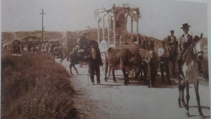 Gente en una mesa de picnic en un campo con un carruaje tirado por caballos. Los invitados comen, algunos saludan; los árboles rodean la escena.