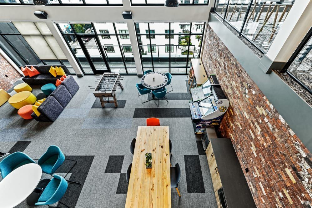 High-angle view of a modern lounge with seating, a foosball table, and a long wooden table. Brick wall on the right at The Verge in Auburn, WA.