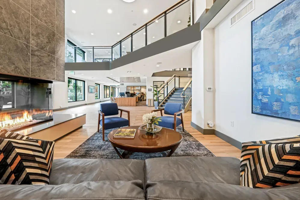 Lobby with fireplace, seating area, and artwork. Natural light, wood floors, and a balcony on the upper level at The Verge in Auburn, WA.