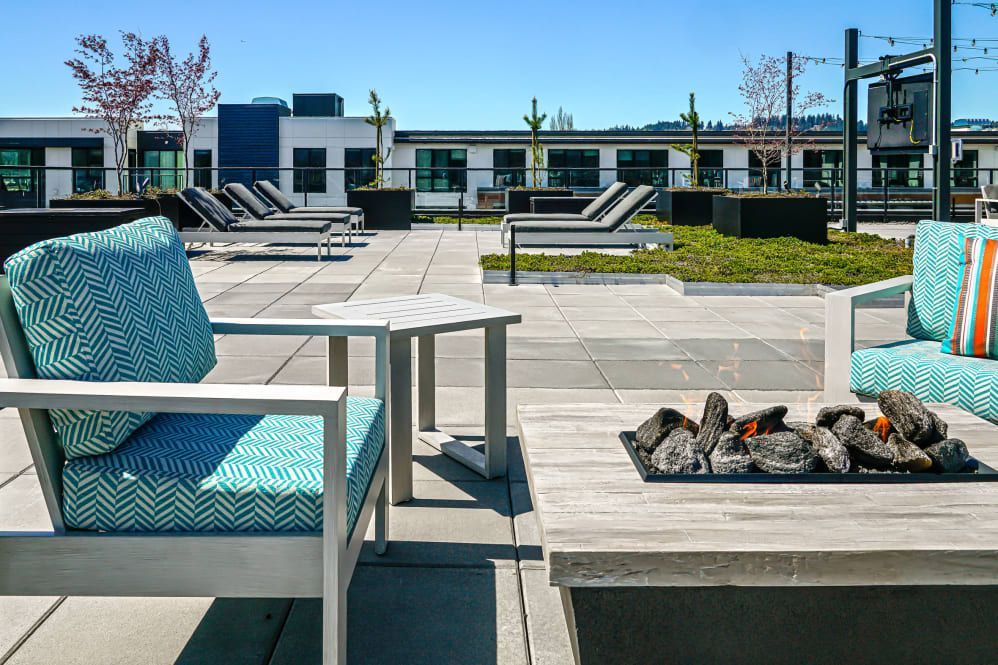 Rooftop patio with lounge chairs, square fire pit, and building in the background on a sunny day at The Verge in Auburn, WA.