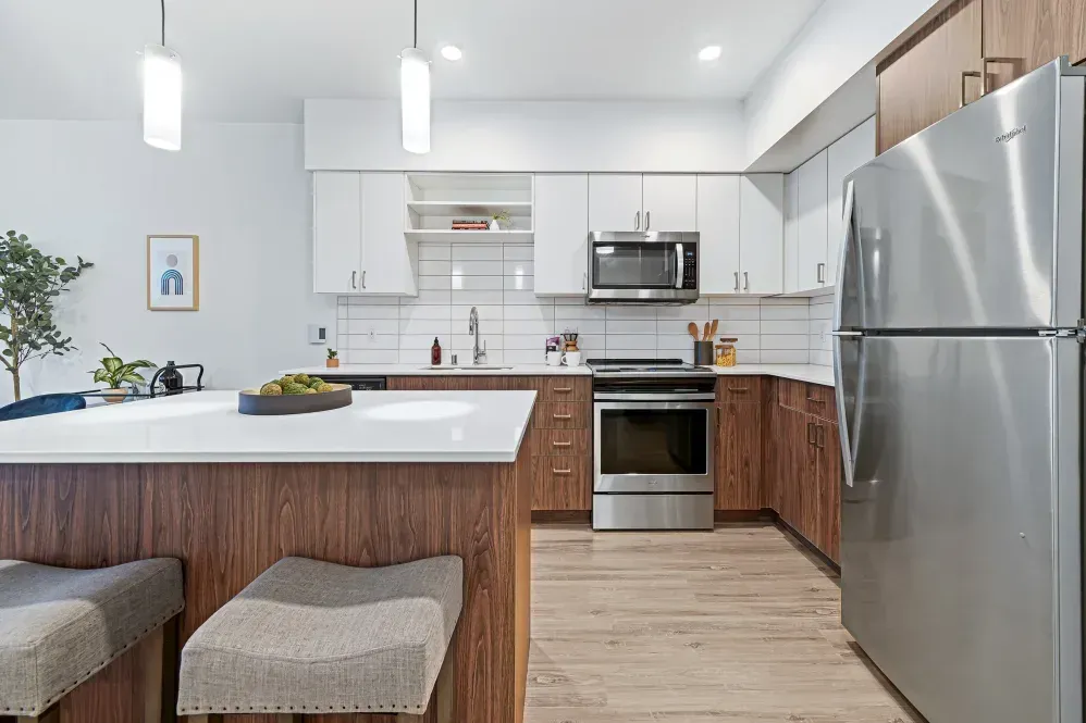 Modern kitchen with a white countertop island, stainless steel appliances, and wood cabinets at The Verge in Auburn, WA.