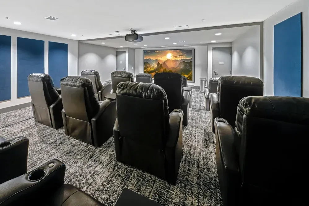 Home theater room with black recliners, screen with landscape art, blue sound panels, gray carpet at The Verge in Auburn, WA.