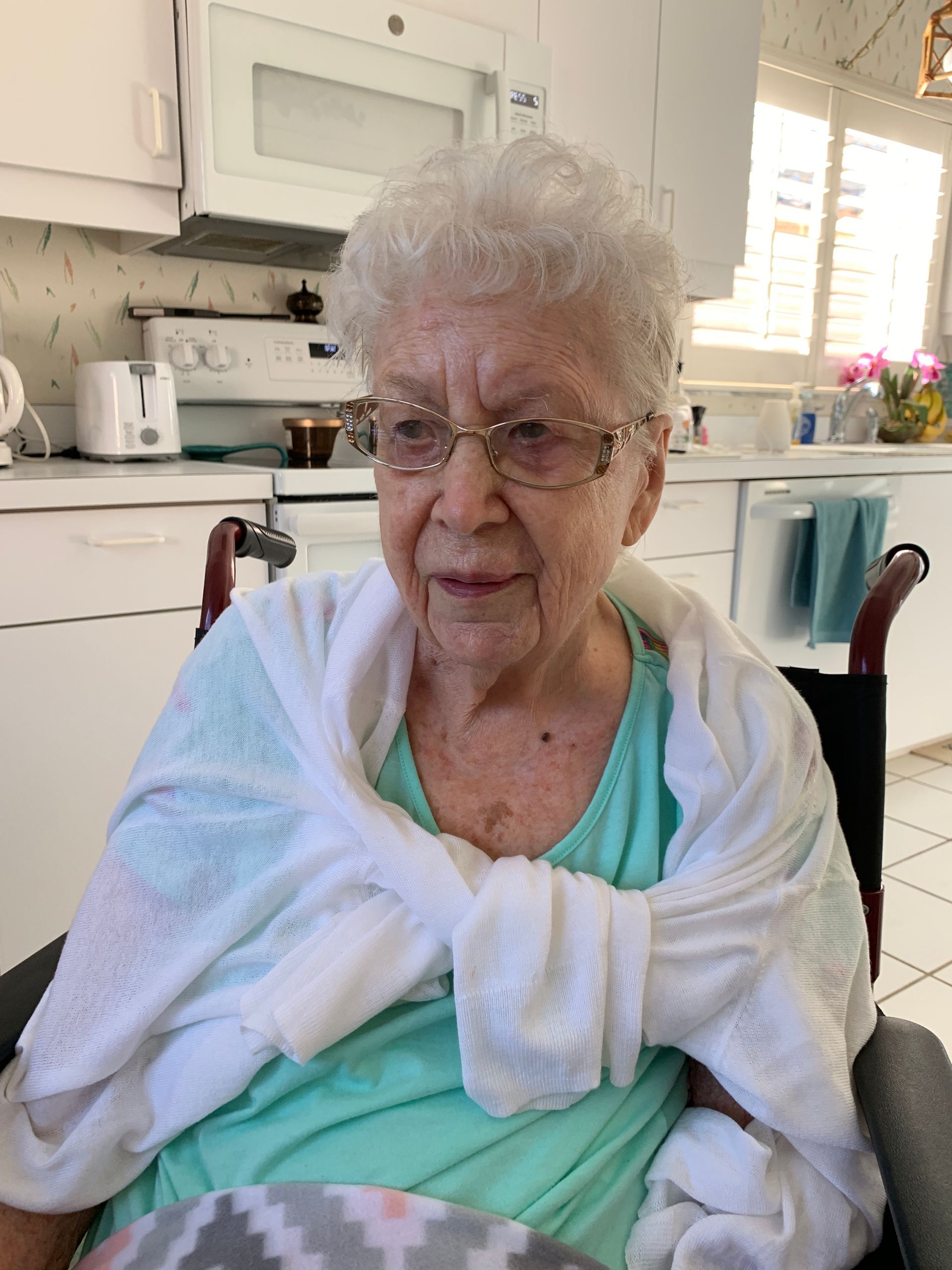 An elderly woman is sitting in a wheelchair wrapped in a towel.