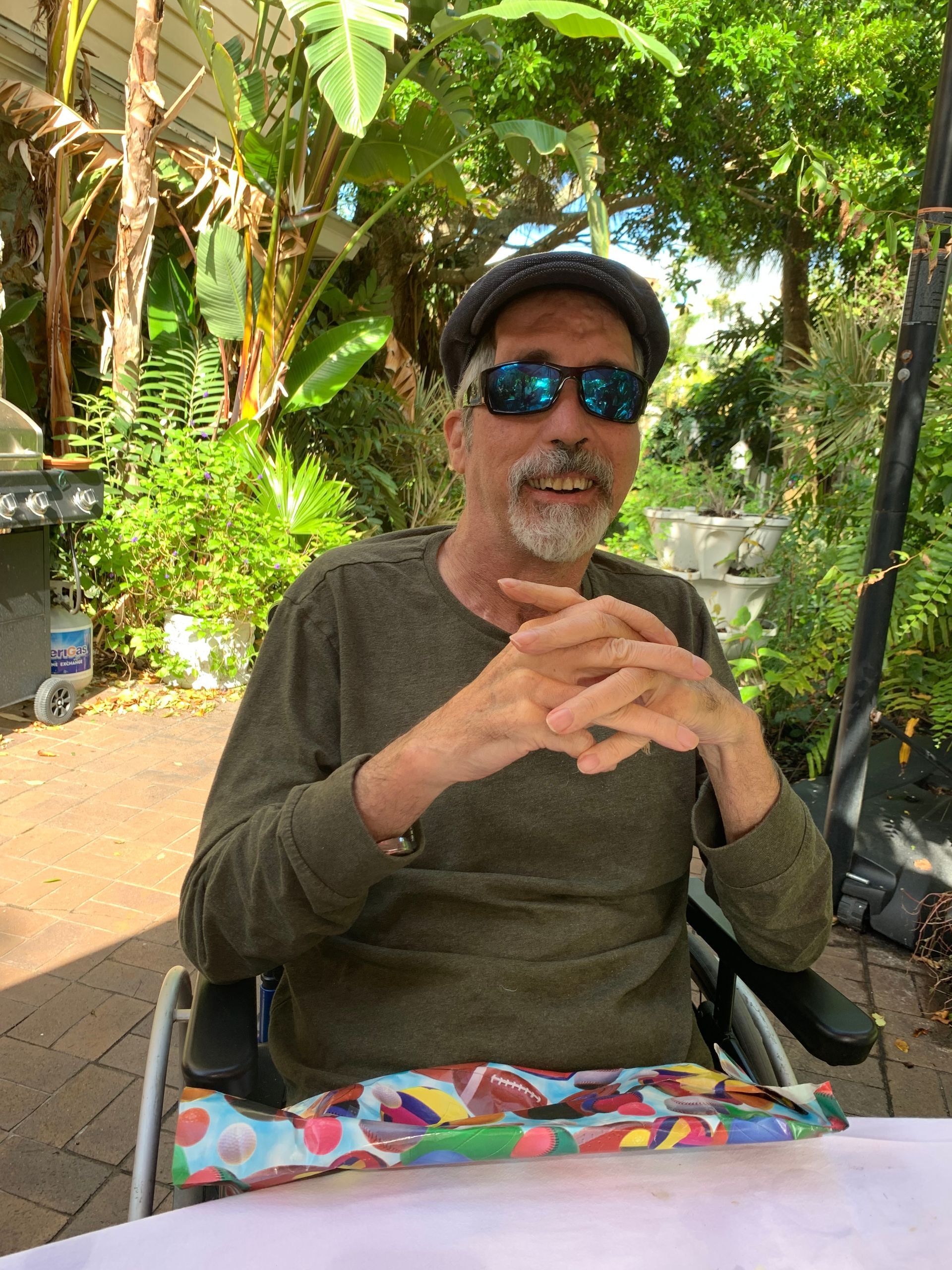 A man in a wheelchair wearing sunglasses and a hat is sitting at a table.