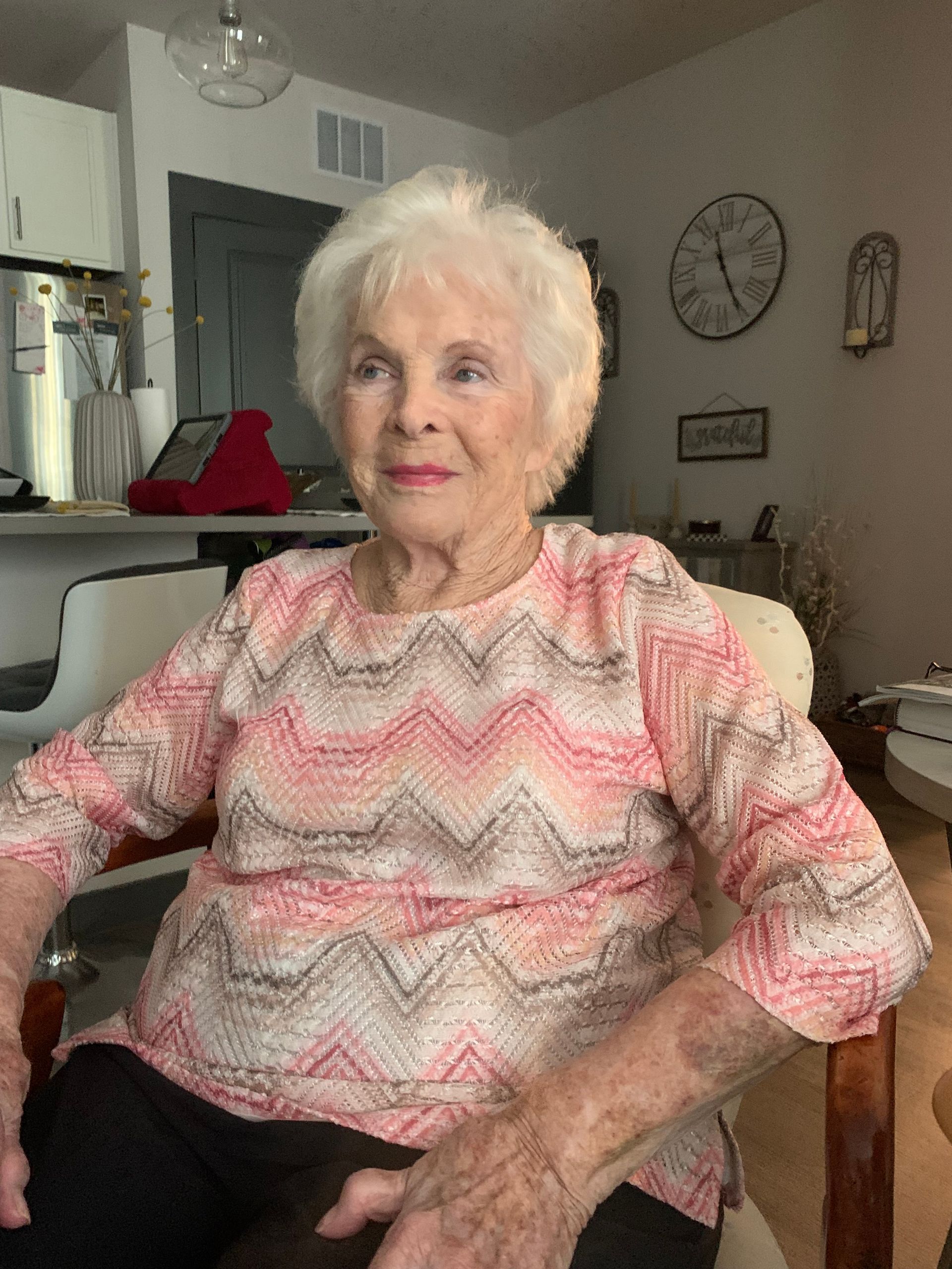 An elderly woman is sitting in a chair in a living room.