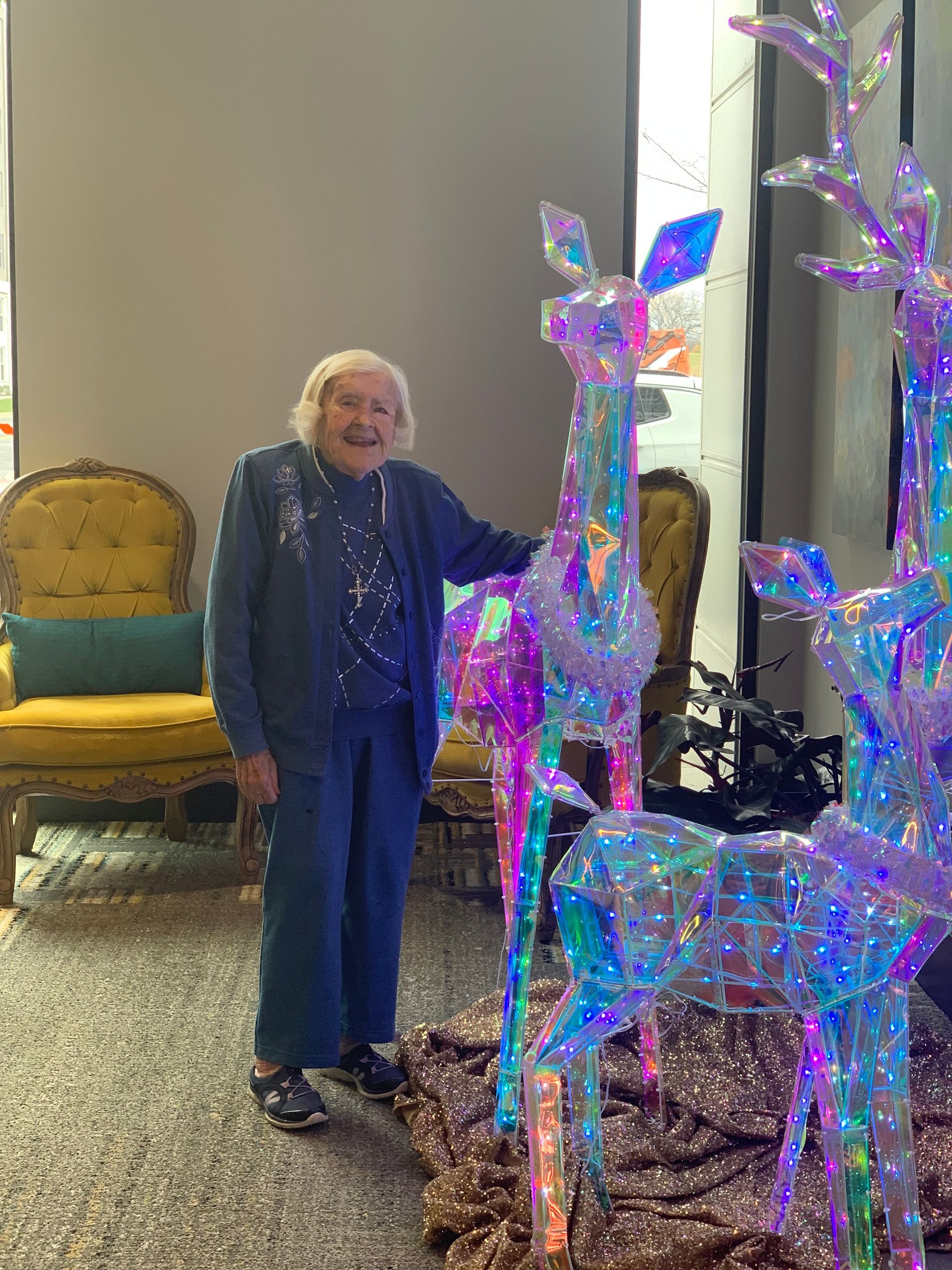 An elderly woman is standing in front of a display of christmas lights.
