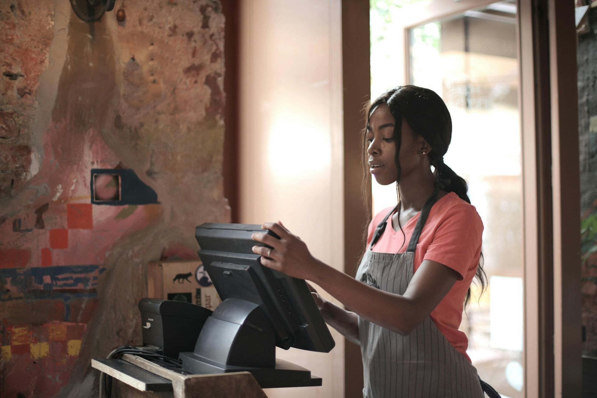 A woman in an apron is using a computer in a restaurant.