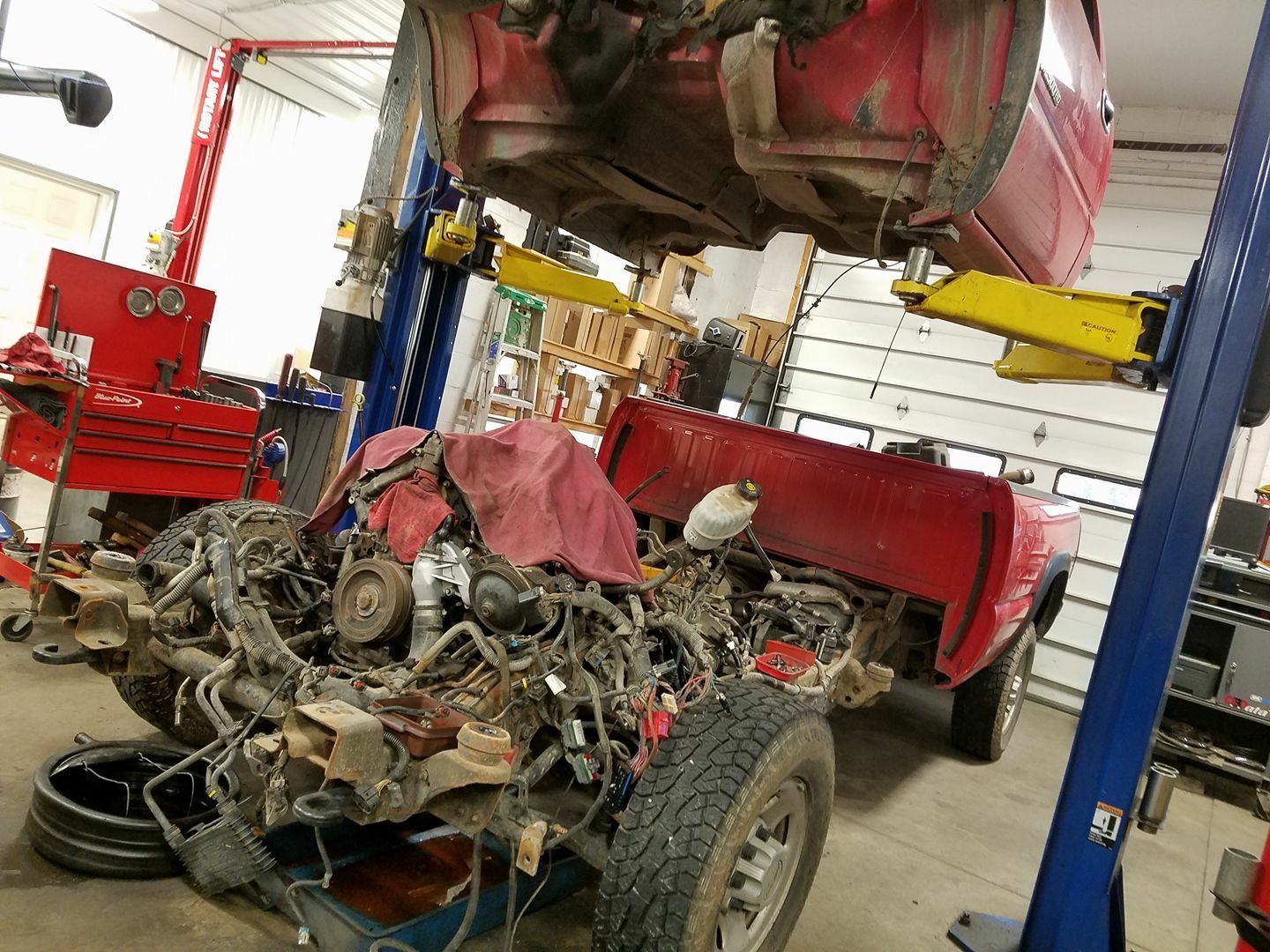 A red pickup truck being worked on in a garage, lifted with engine removed | Central Auto Works