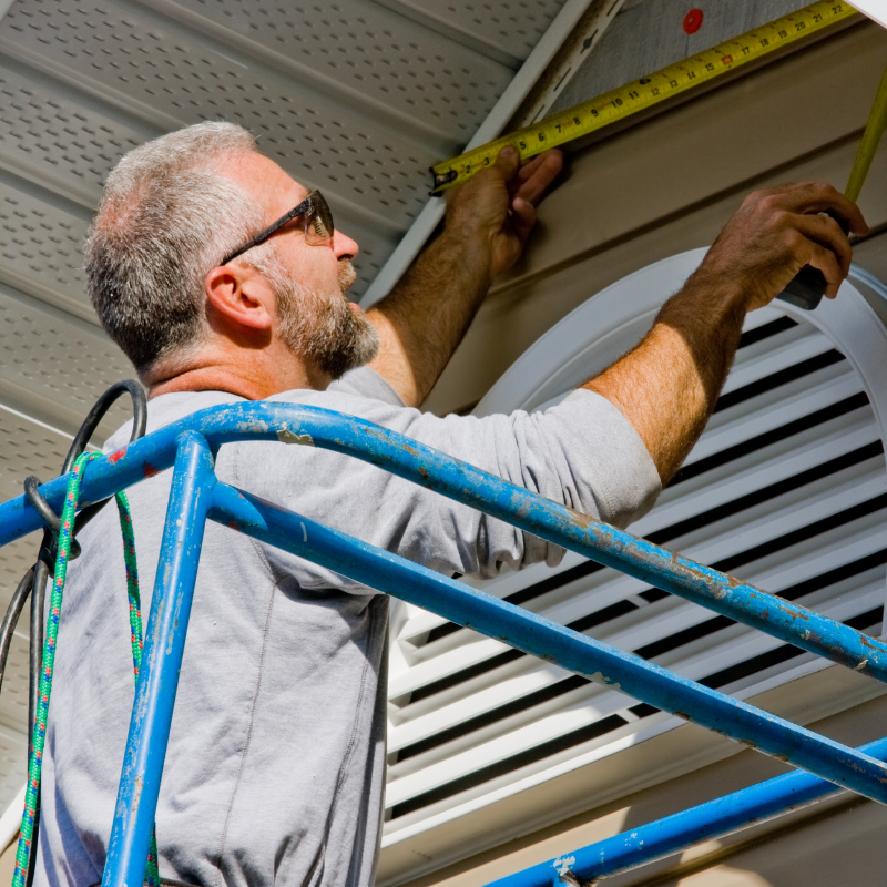 A man standing on a scaffolding measuring something with a tape measure