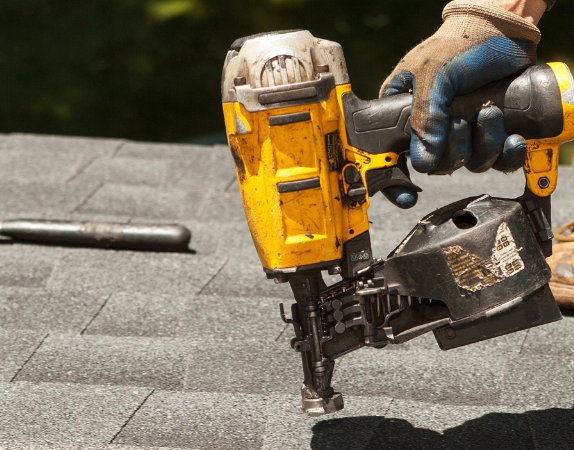 A man is using a drill to fix a gutter on a house