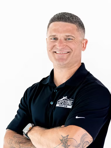 A man in a black shirt is smiling with his arms crossed.