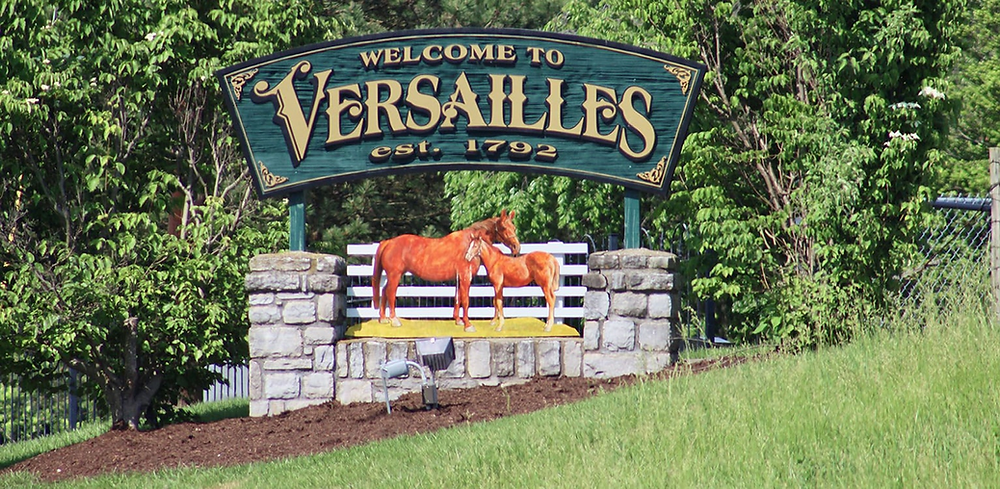 A welcome to versailles sign with two horses on it