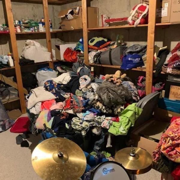 Cluttered basement storage with clothes, shelves of items, and drum cymbals in the foreground.