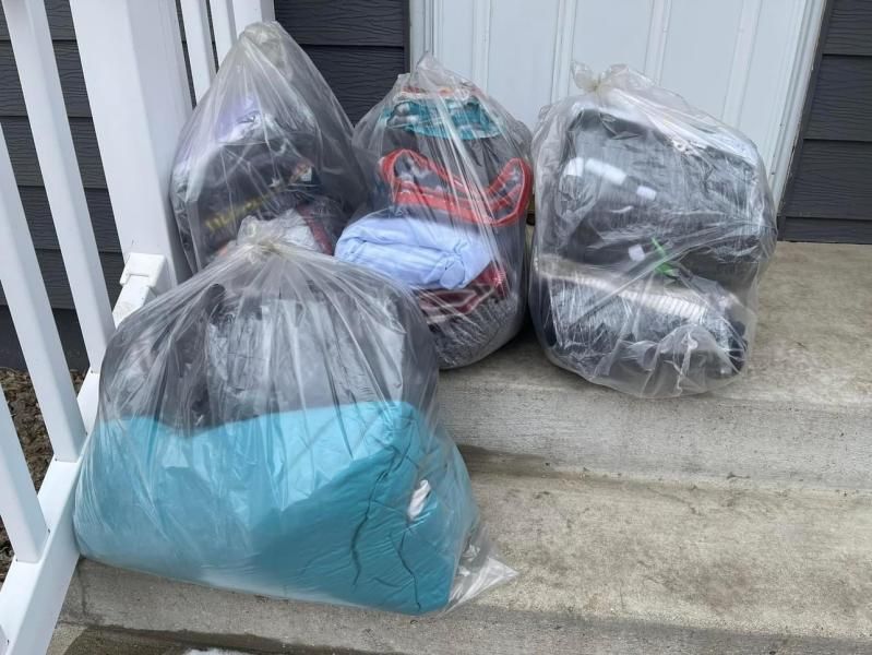 Five plastic bags filled with clothes on a concrete porch step.