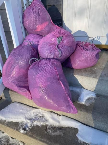Several purple mesh bags, filled, on snowy steps.