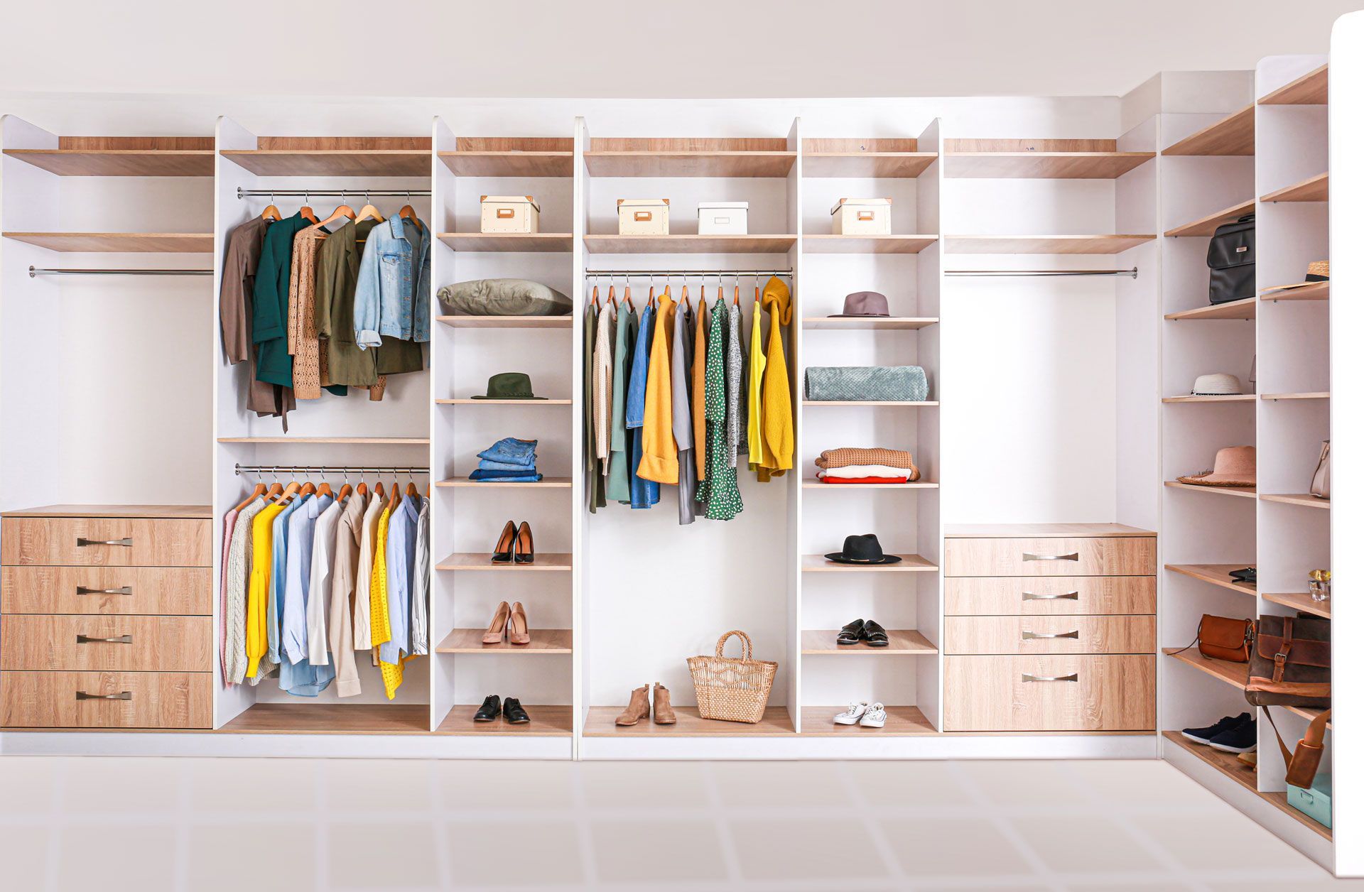 Walk-in closet with light wood shelving, clothes, shoes, and accessories organized on shelves and hanging rods.