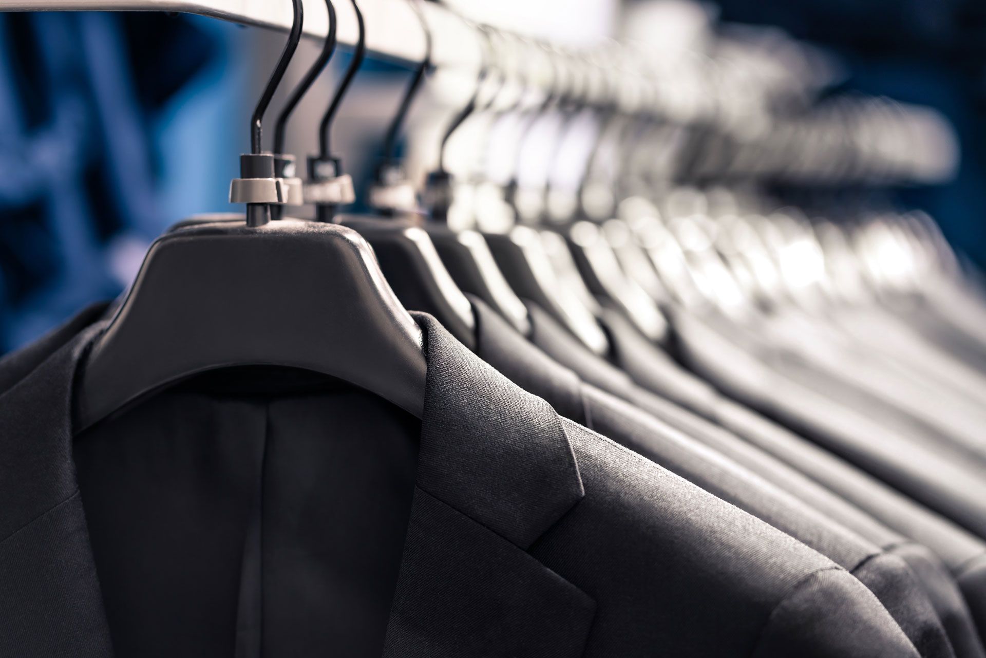 Row of black suit jackets hanging on a clothing rack, in a store.