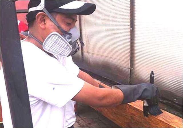 Un hombre con máscara y guantes está trabajando en un trozo de madera