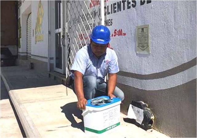 Un hombre con casco azul está arrodillado con un balde frente a un cartel que dice clientes