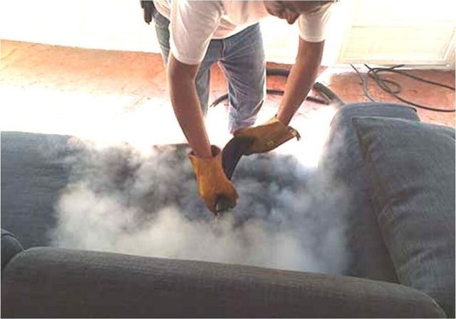 Un hombre está limpiando un sofá con una aspiradora.