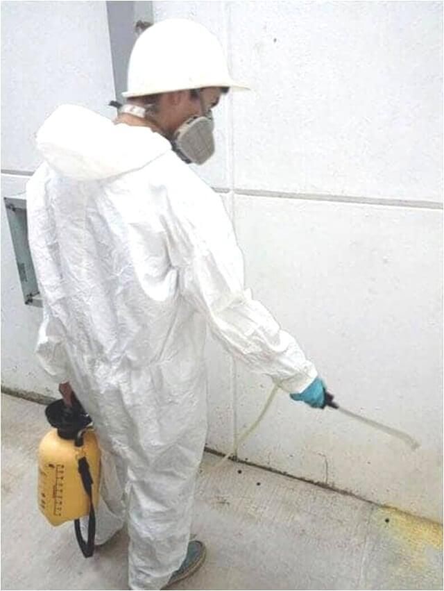 Un hombre con un mono blanco rociando una pared con un rociador amarillo