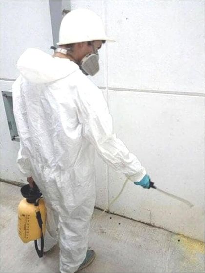 Un hombre con un mono blanco rociando una pared con un rociador amarillo