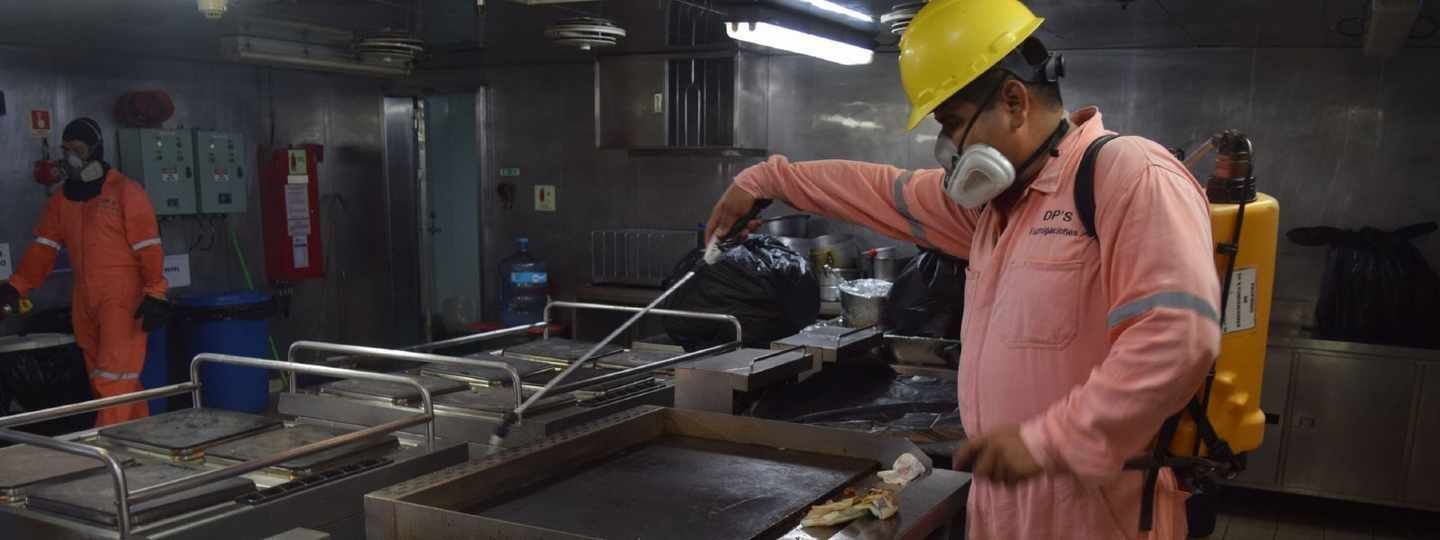 Un hombre que lleva un casco y una máscara está limpiando una estufa en una cocina.