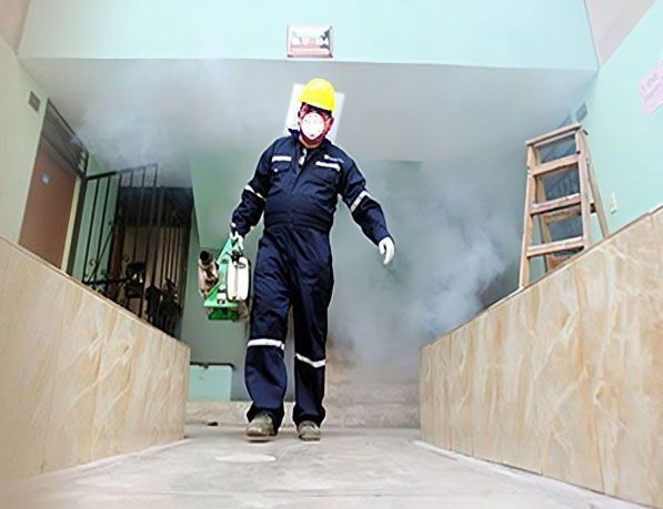 Un hombre que lleva casco y mono está desinfectando un edificio.