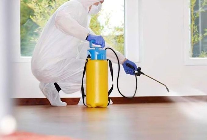 Un hombre con traje protector está rociando una habitación con un pulverizador.
