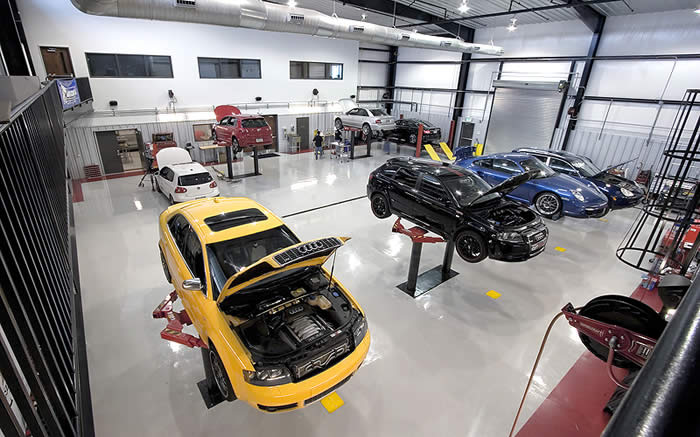 A yellow car is sitting in a garage with its hood open.