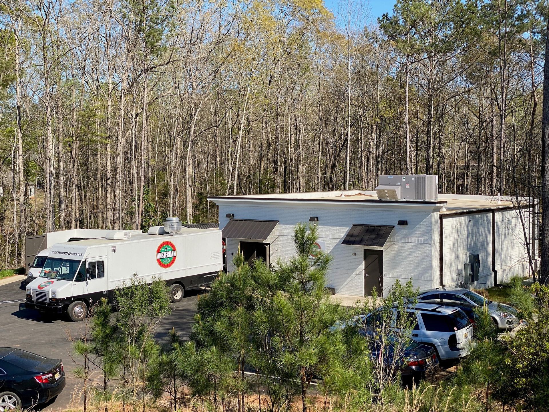 A white truck is parked in front of a building in the woods.