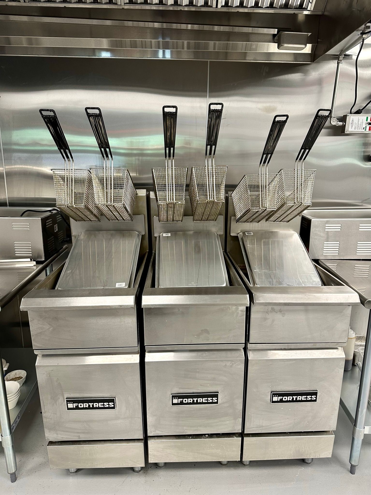 Three stainless steel fryers are stacked on top of each other in a kitchen.