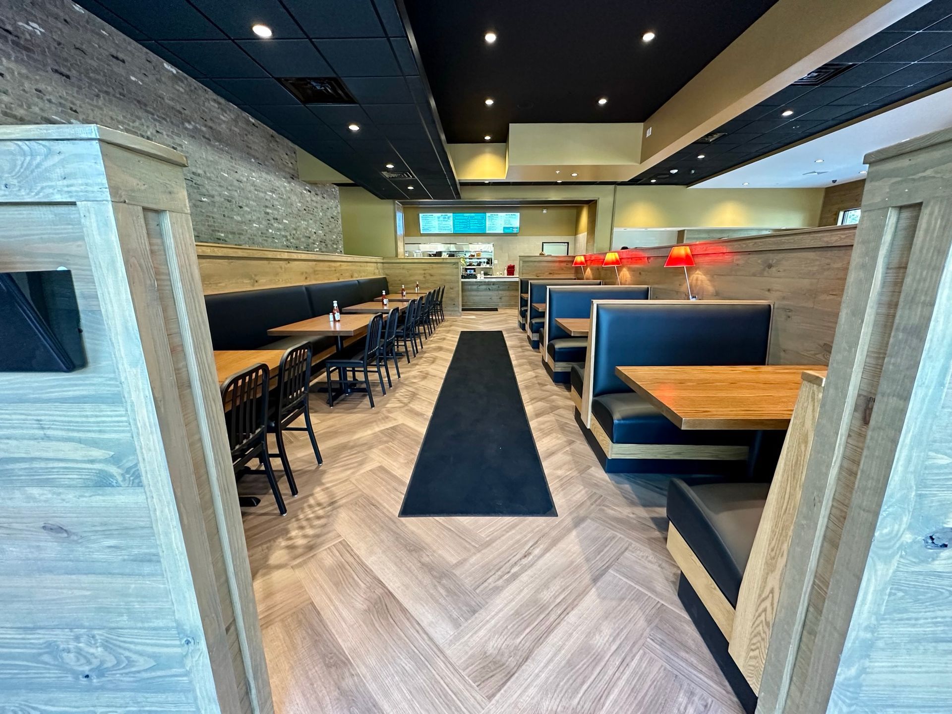 A restaurant with tables and benches and a black mat on the floor.