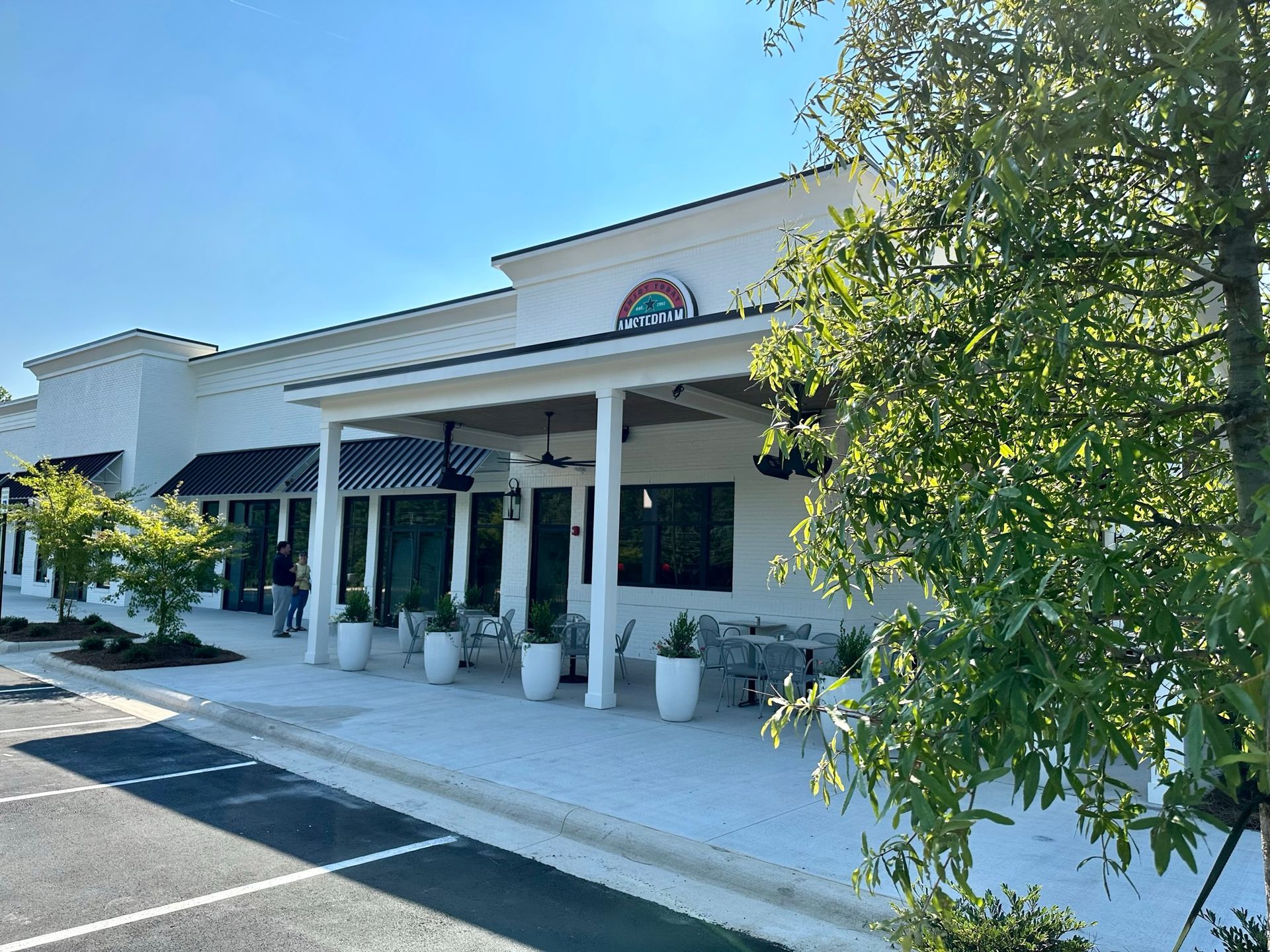 A white building with a covered porch and a tree in front of it.