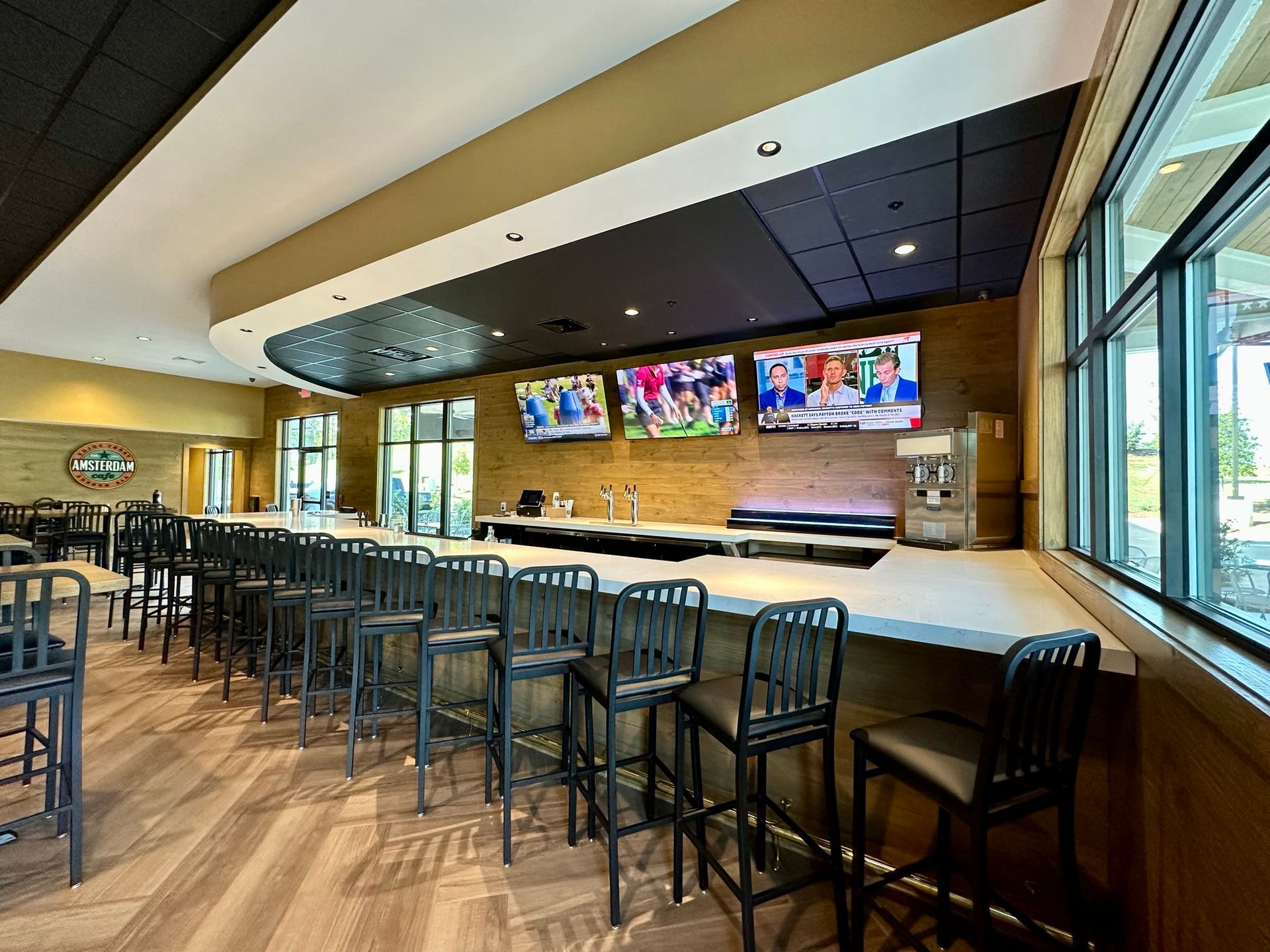 A long bar with stools and televisions in a restaurant.
