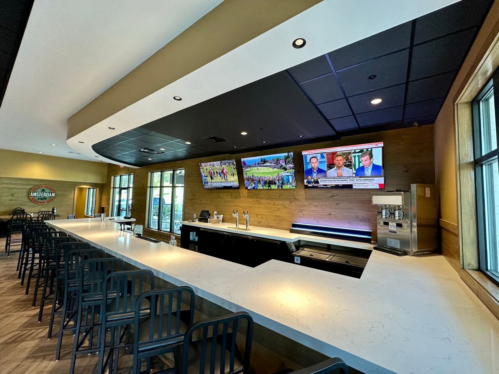 A long bar in a restaurant with a lot of televisions on the wall.