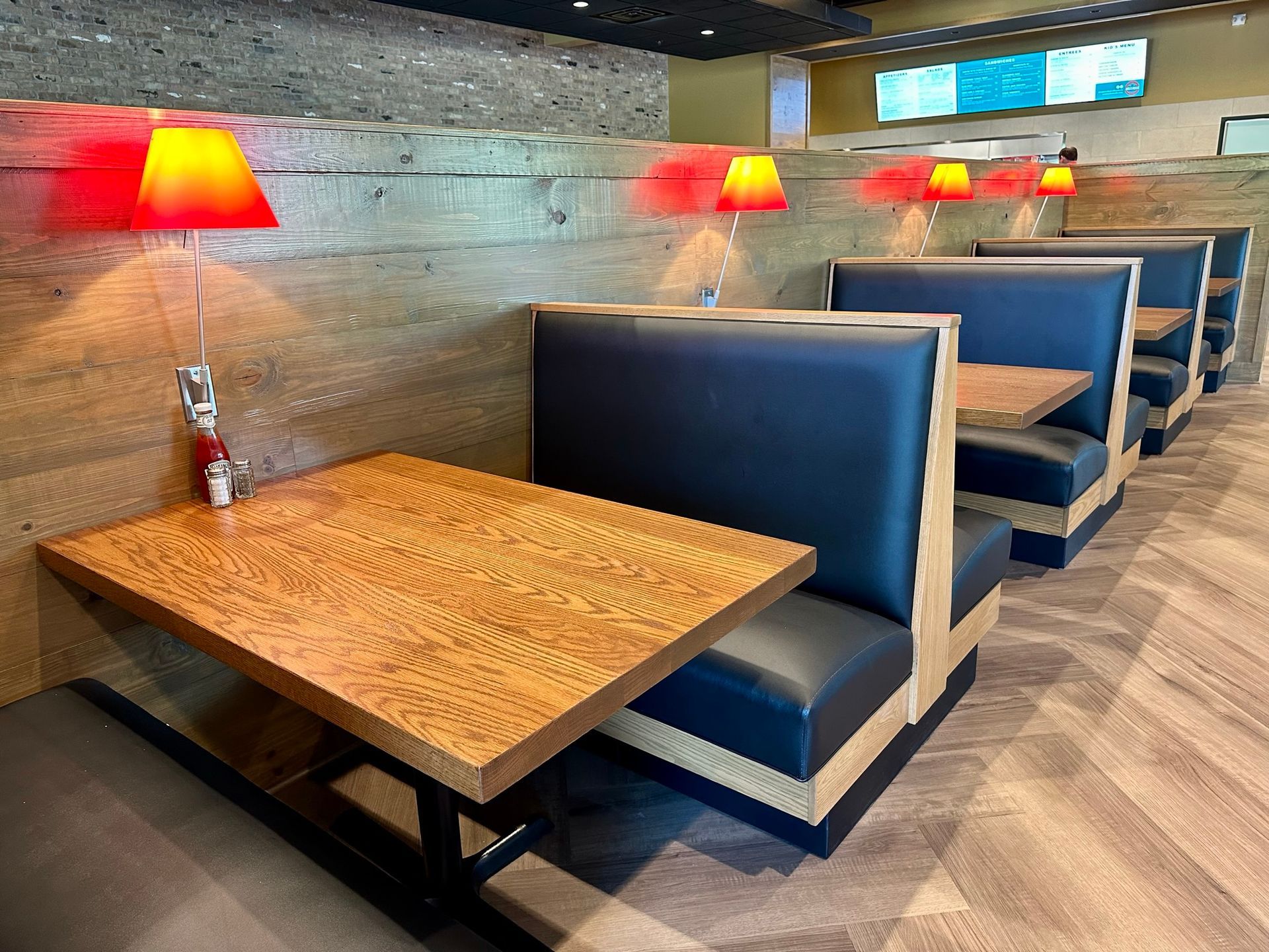 A row of booths in a restaurant with tables and lamps.