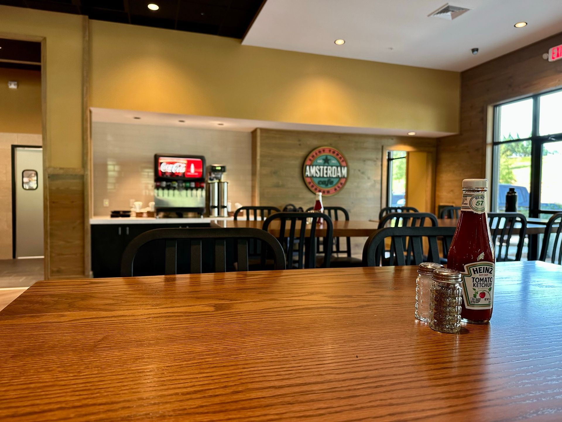 A bottle of ketchup sits on a wooden table in a restaurant.