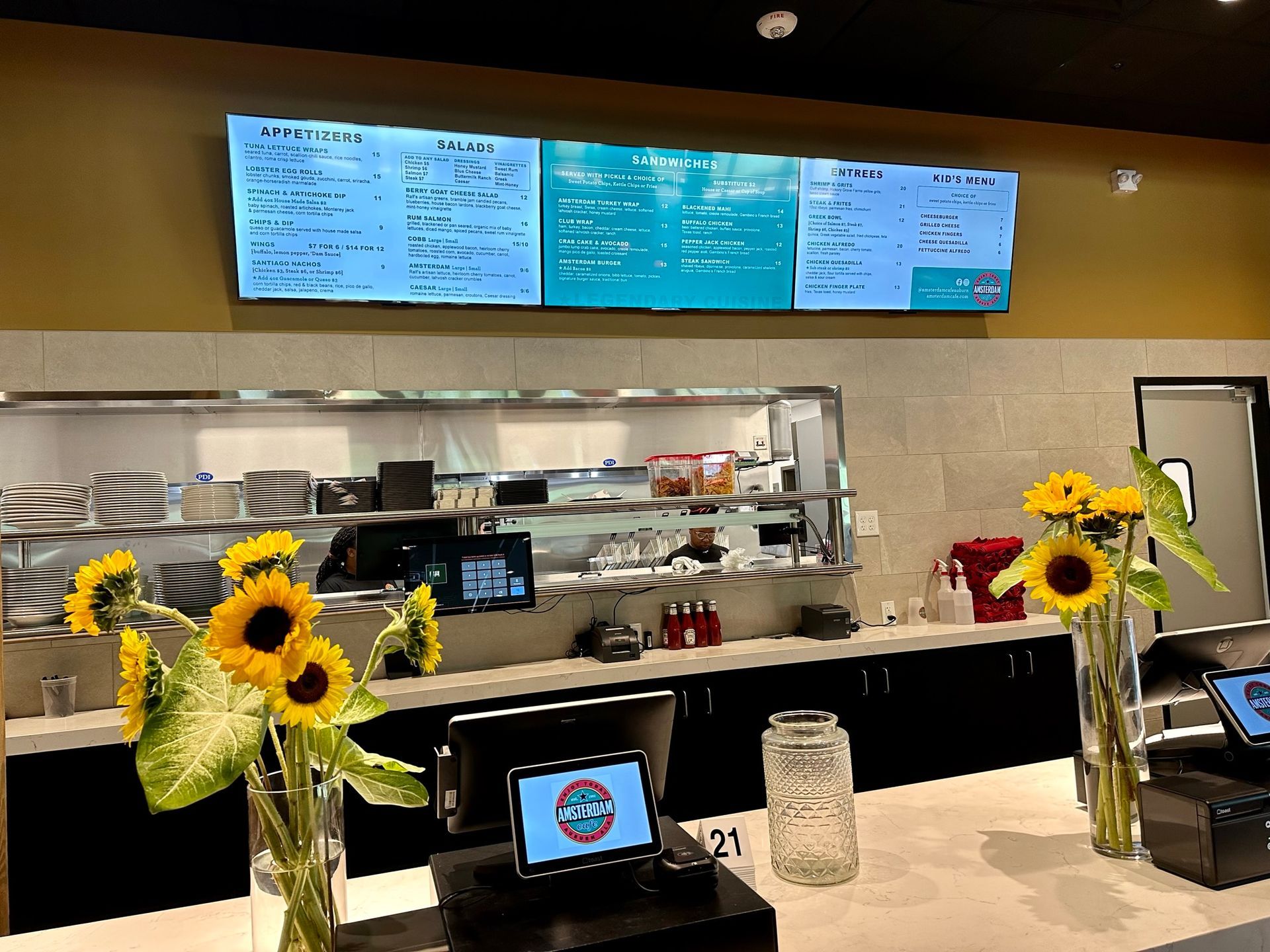 A restaurant with sunflowers on the counter and a menu on the wall.