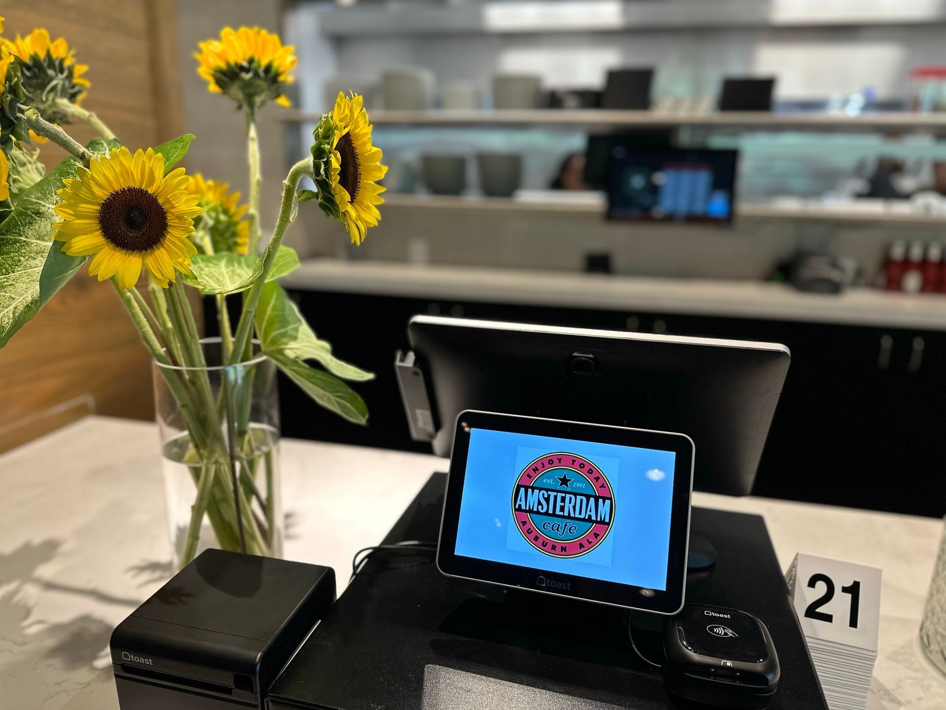 A computer monitor is sitting on a counter next to a vase of sunflowers.