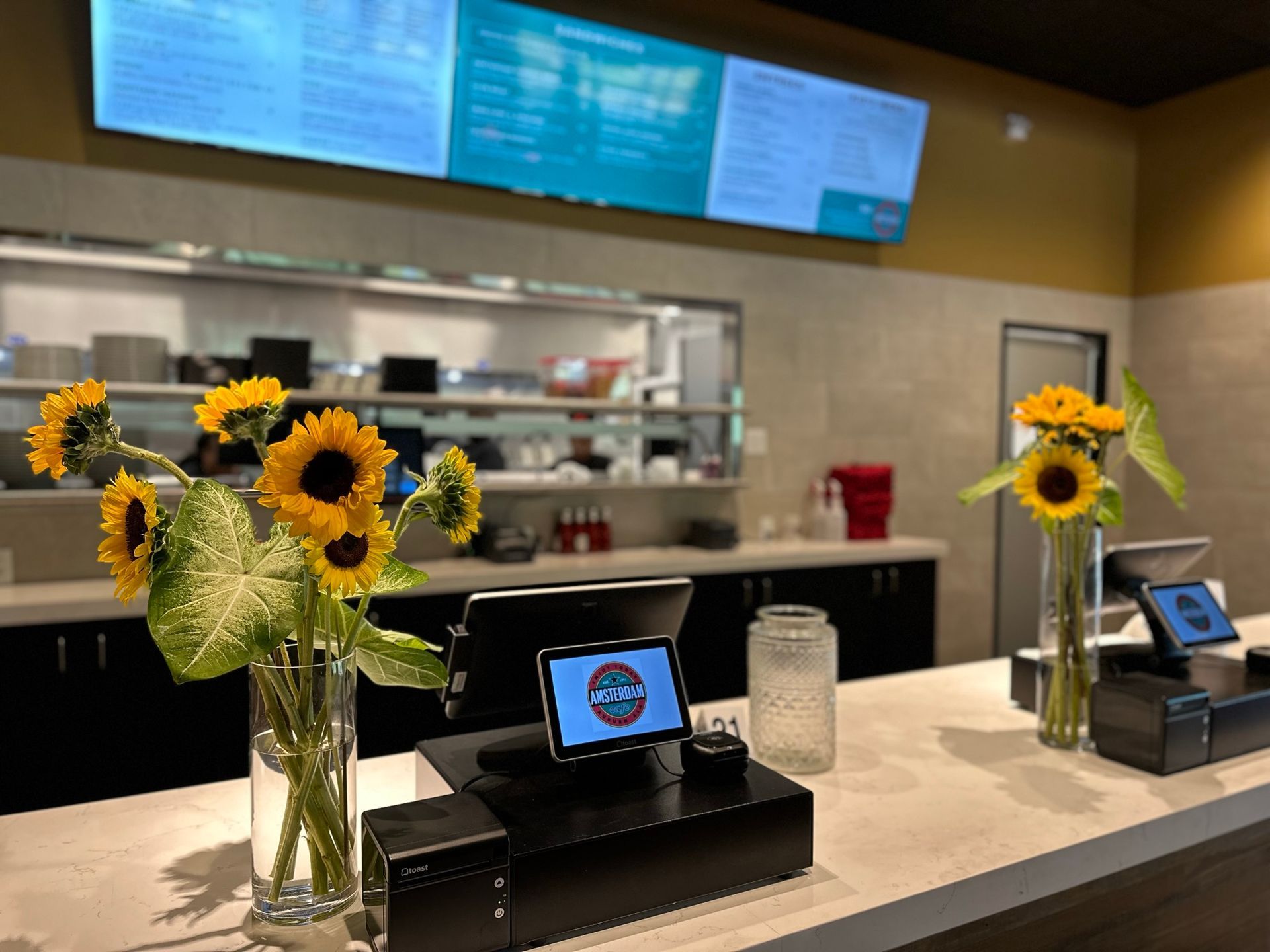 A counter in a restaurant with sunflowers in vases on it.