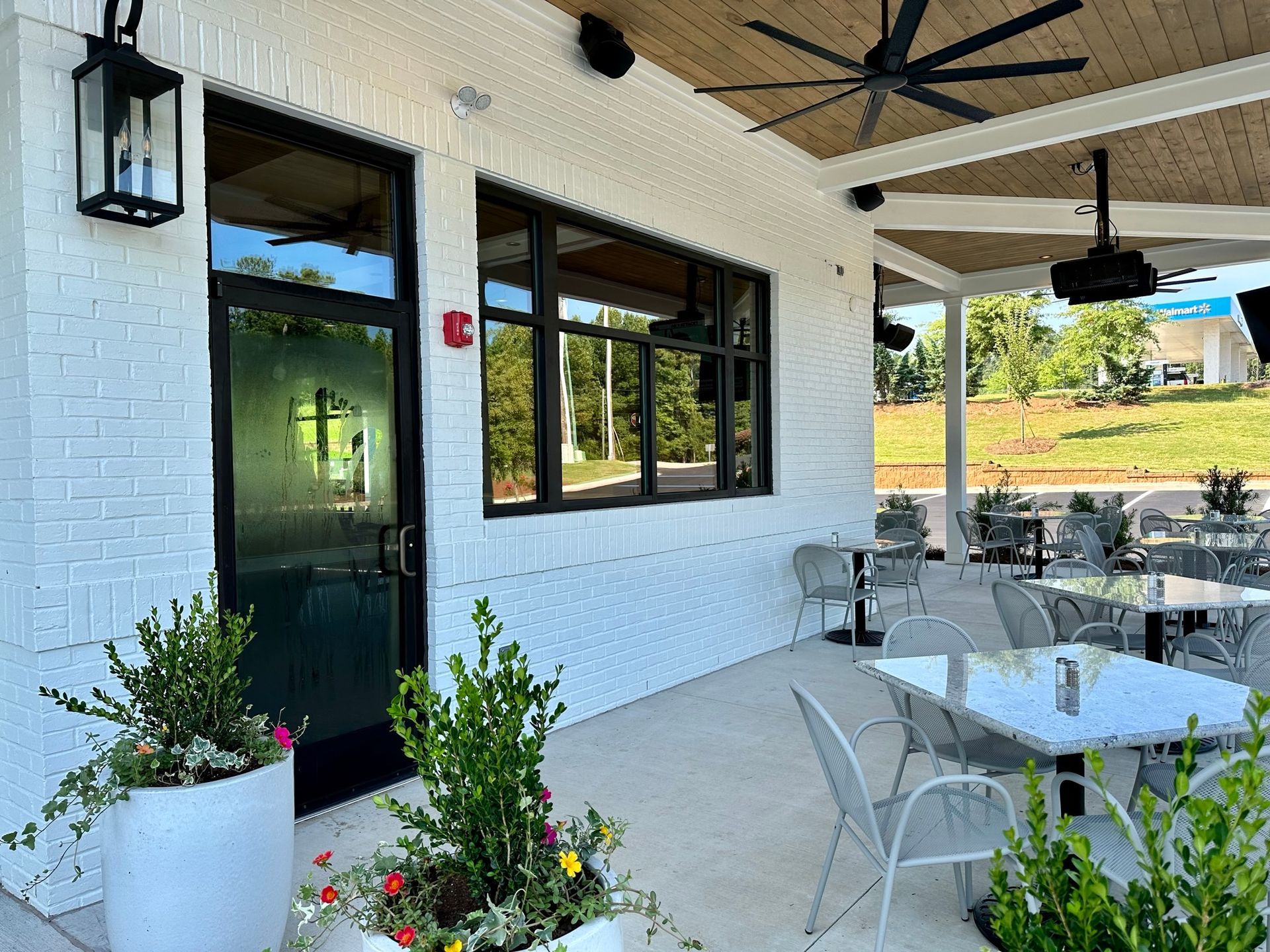 There are tables and chairs outside of a restaurant with a ceiling fan.