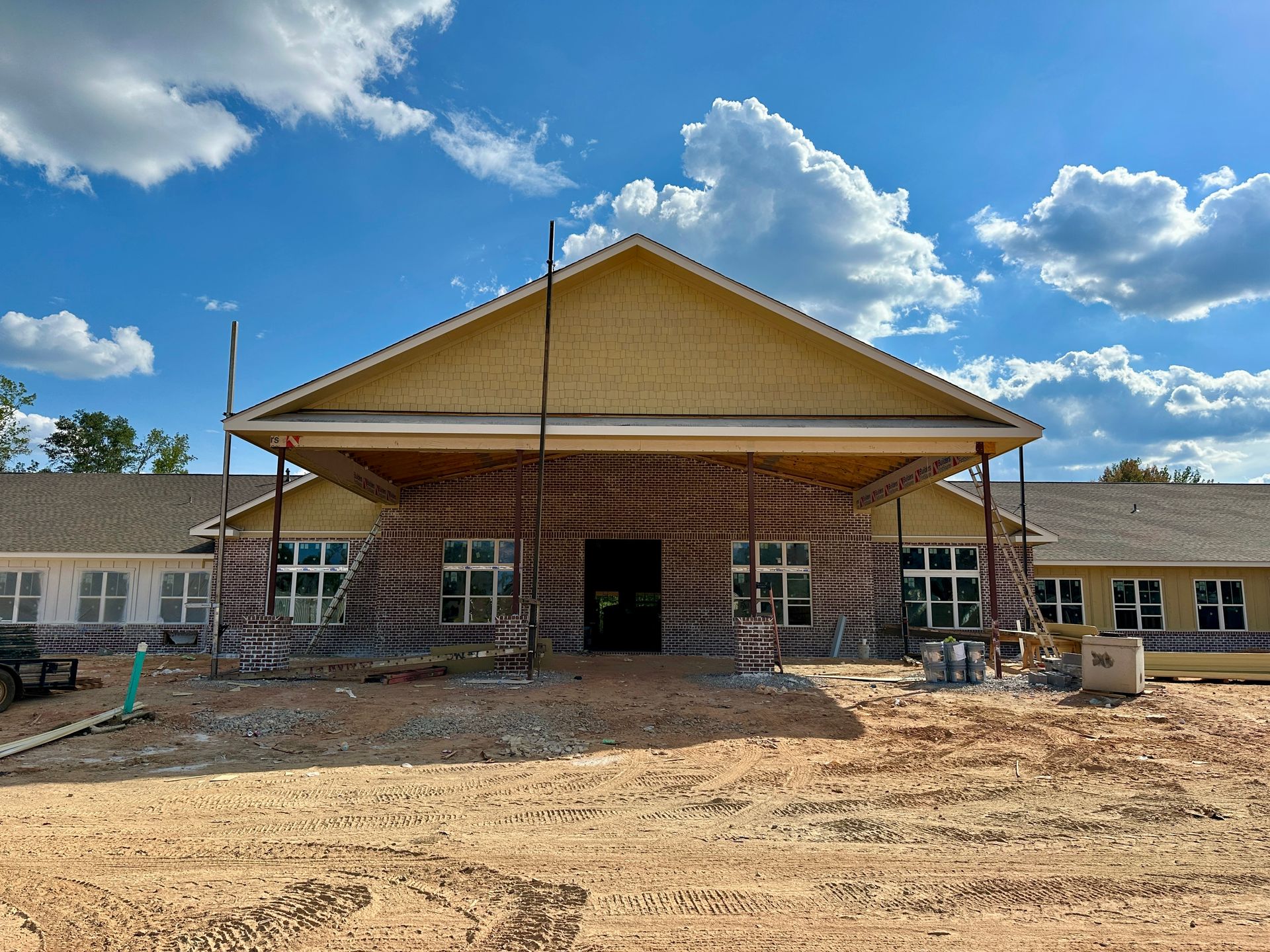 Building under construction with a large entrance; brown and tan colors; cloudy blue sky.
