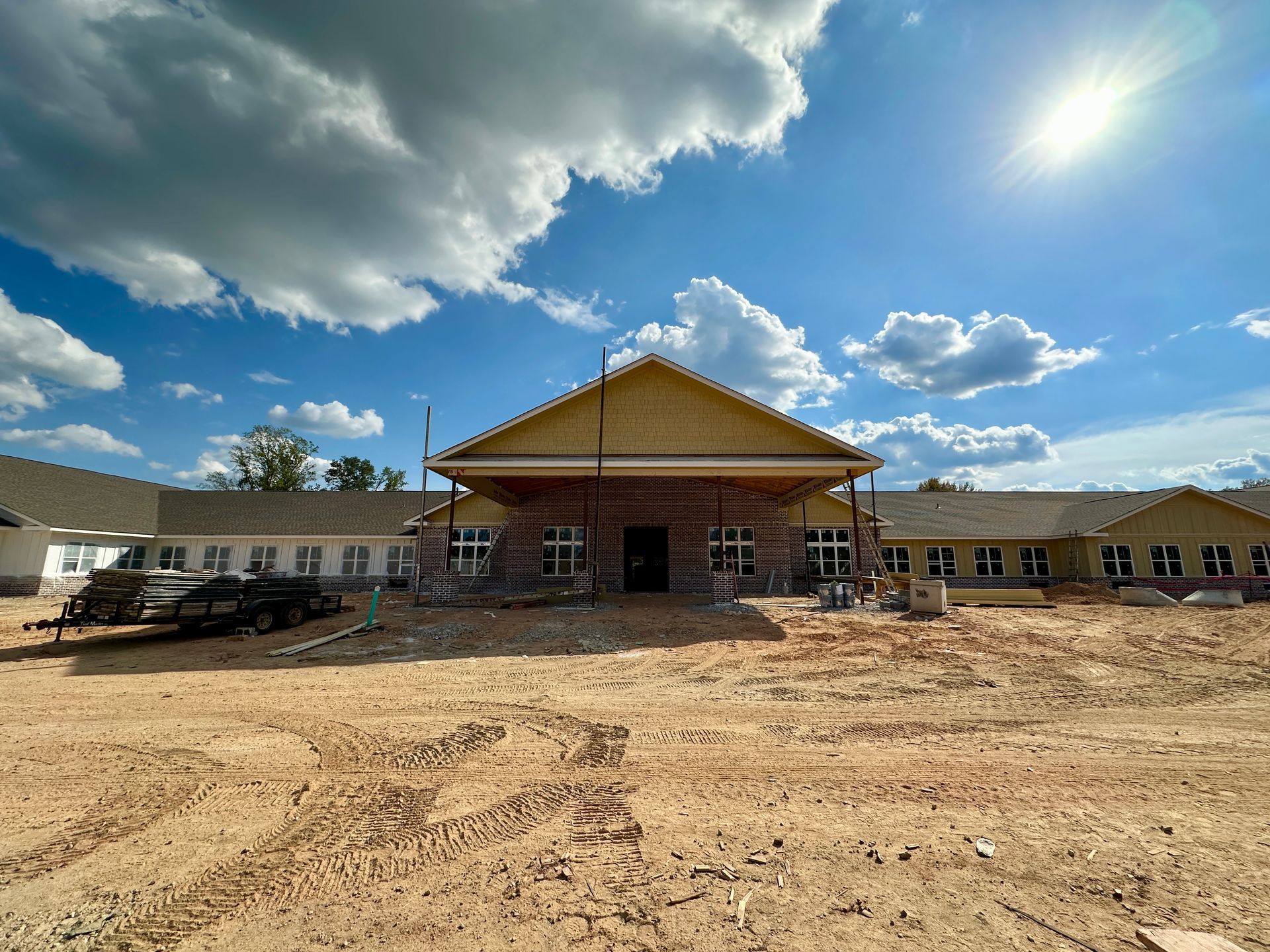 Building under construction on a sunny day with a cloudy sky. Dirt and equipment are visible.