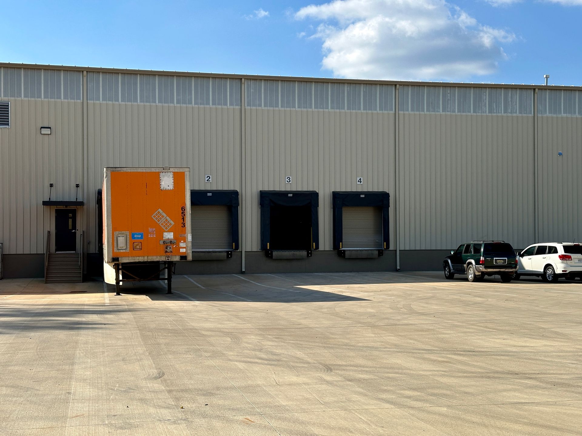 A truck is parked in front of a warehouse with cars parked in front of it.