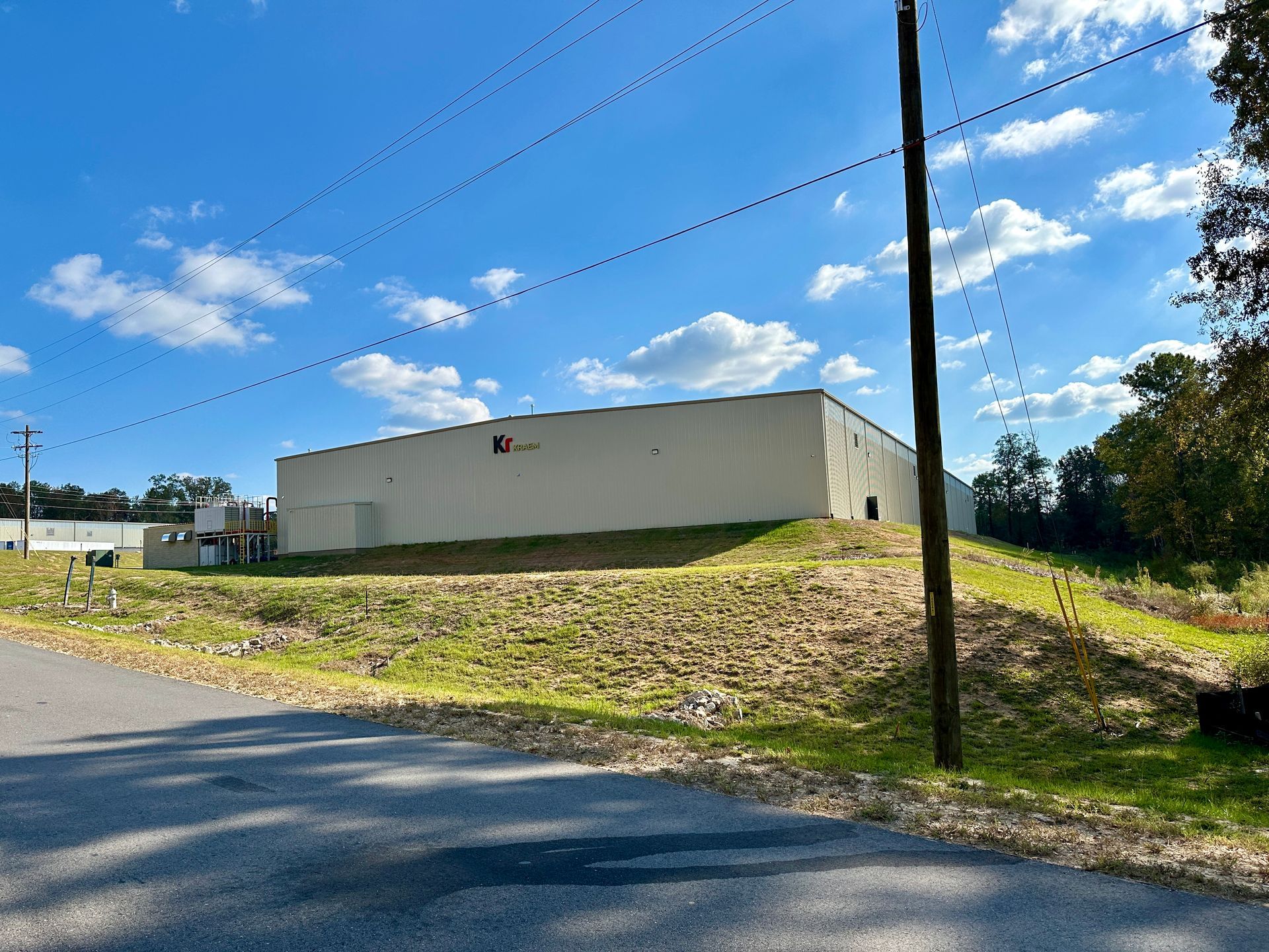 A large white building is sitting on top of a grassy hill next to a road.