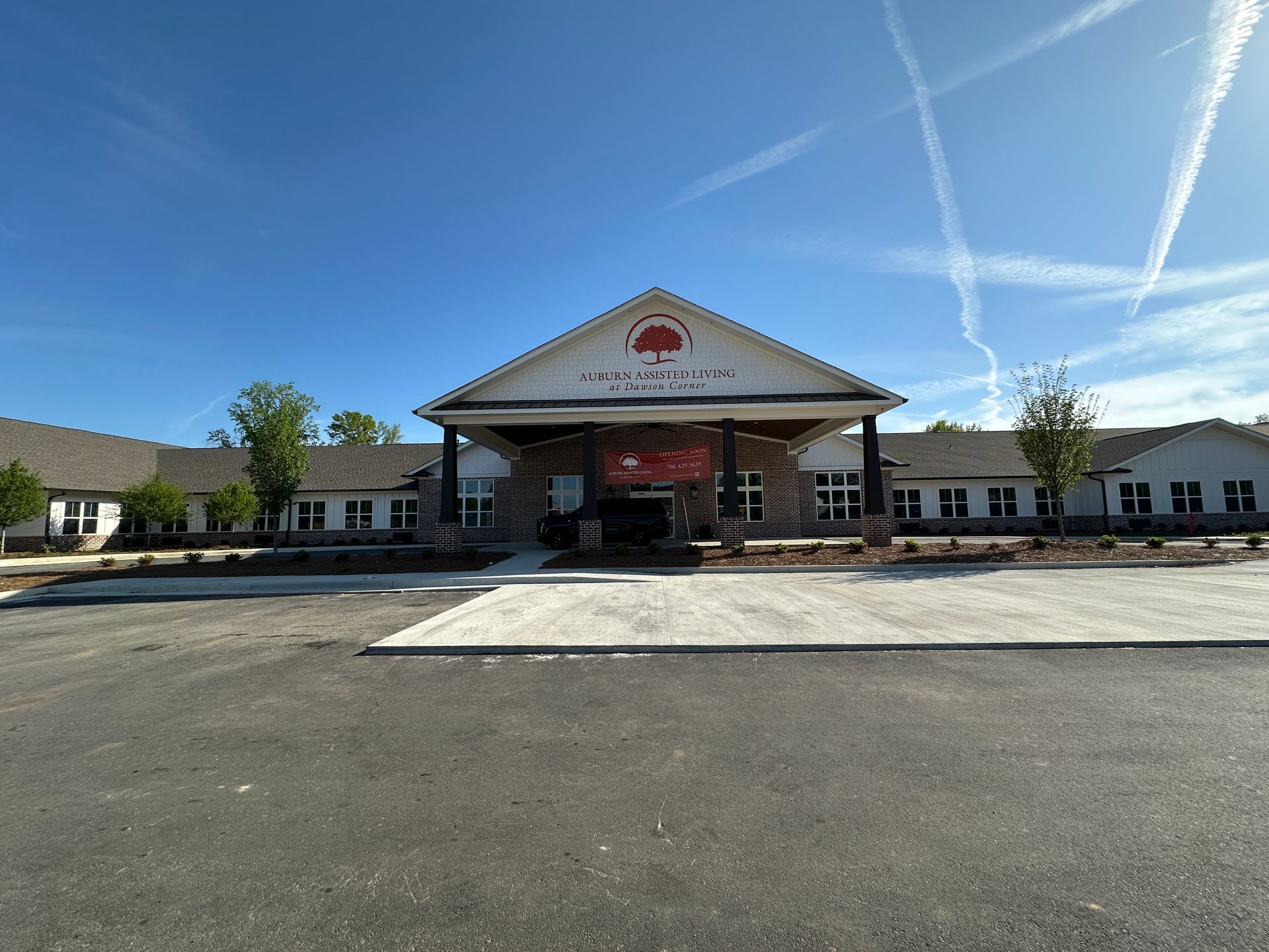A single-story, tan, L-shaped building with a peaked entrance under a clear blue sky, viewed from a paved parking lot.