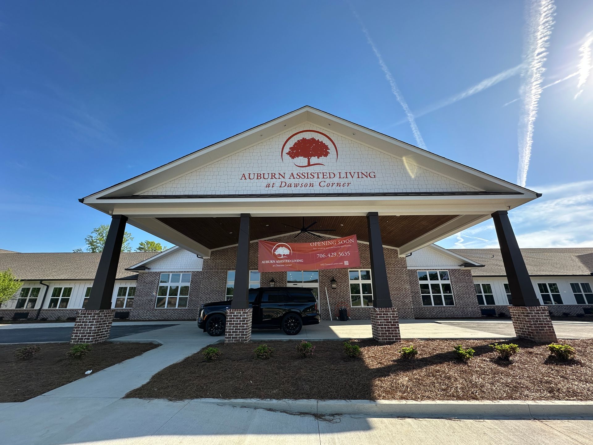 A bright, sunny view of the entrance to the Auburn Assisted Living facility, featuring a large porch and brown brick.
