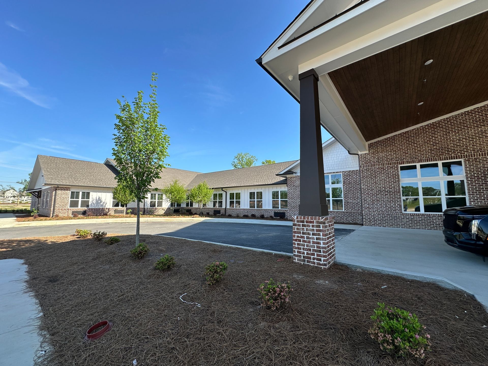 A modern, one-story brick building with a covered entrance, a paved driveway, and landscaping with mulch and young trees.