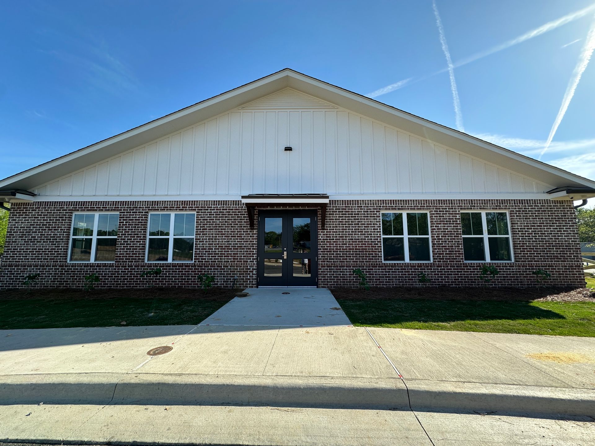 A front view of a single-story building with a white gabled roof and dark brick facade, featuring a central double door.